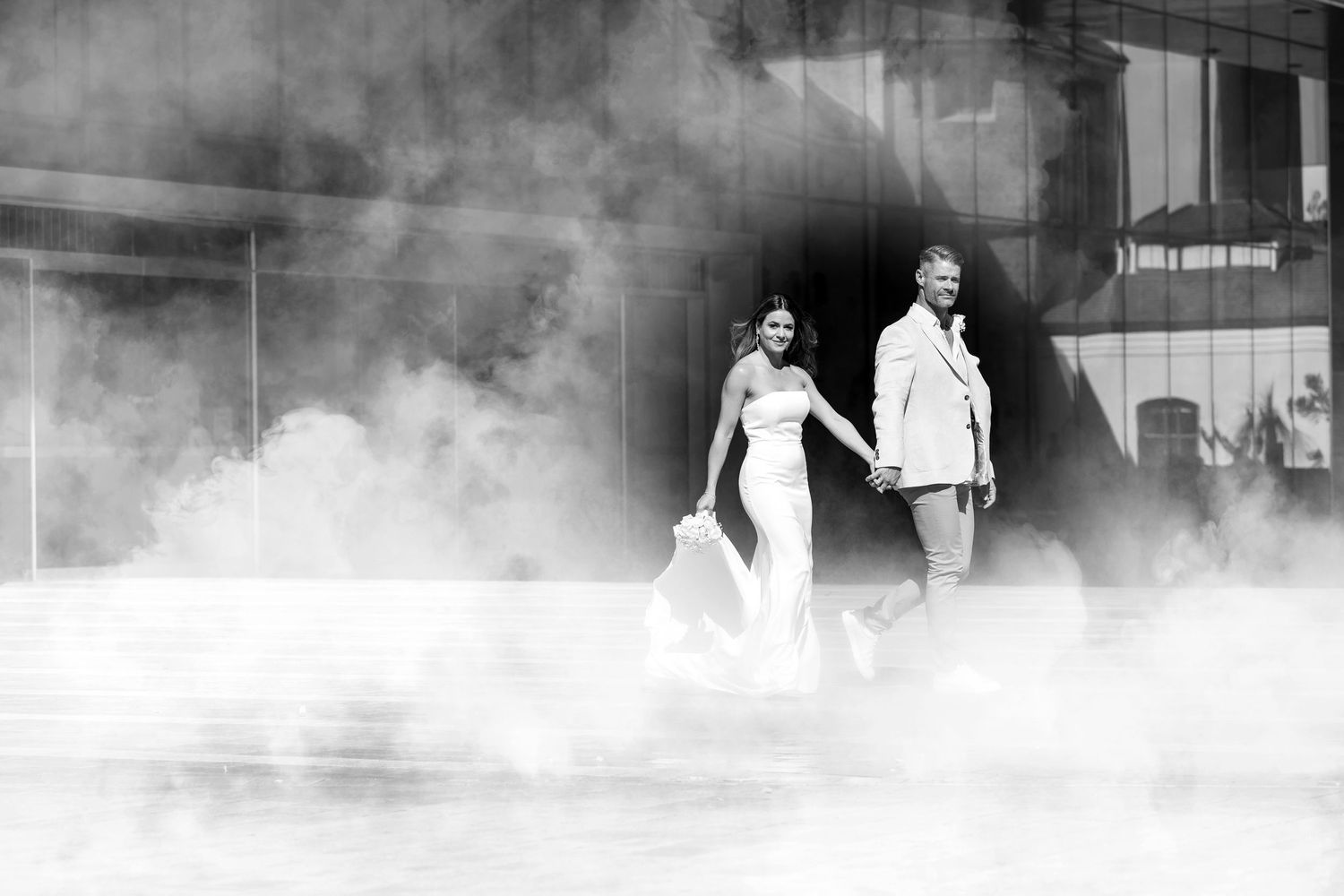 Black and white photo of a bride and groom walking through dramatic fog at their wedding venue.