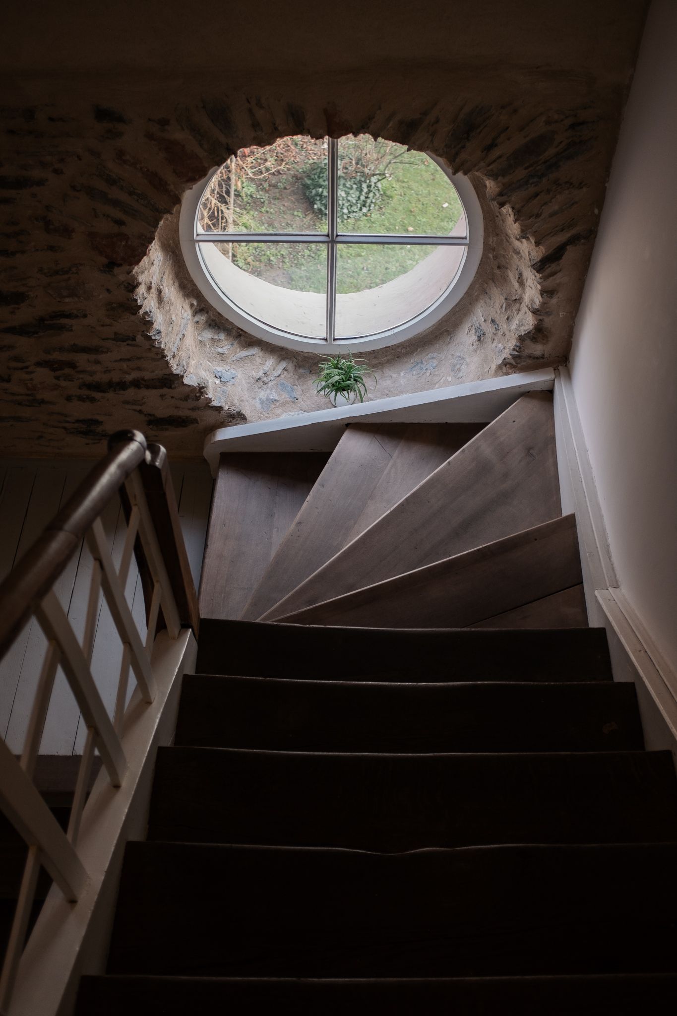 A series of oval windows in a dark stairwell cast natural light down spiral stairs in an architectural sequence.