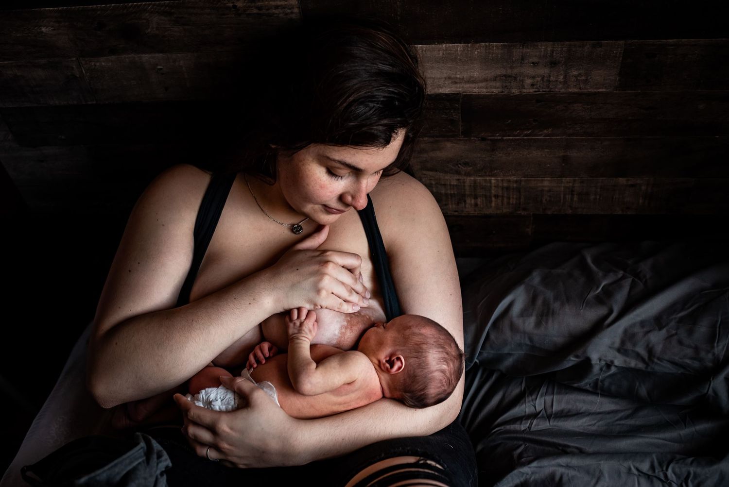 A tender moment captured as a mother breastfeeds her newborn baby in a dimly lit room with wooden walls.