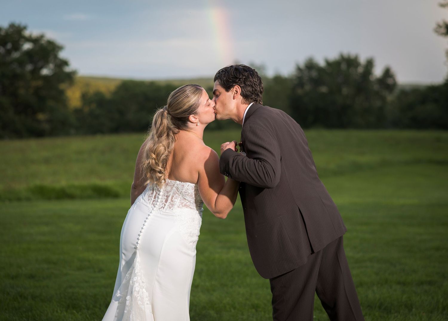 Newlyweds share an intimate moment outdoors with autumn foliage and rustic architecture in background.