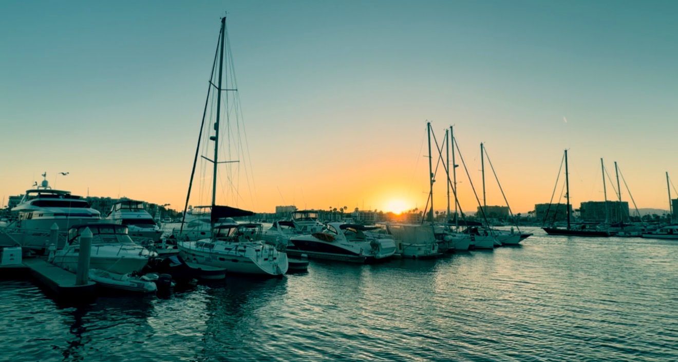Sailboats and yachts docked in a marina at golden sunset with calm water reflections and clear sky.