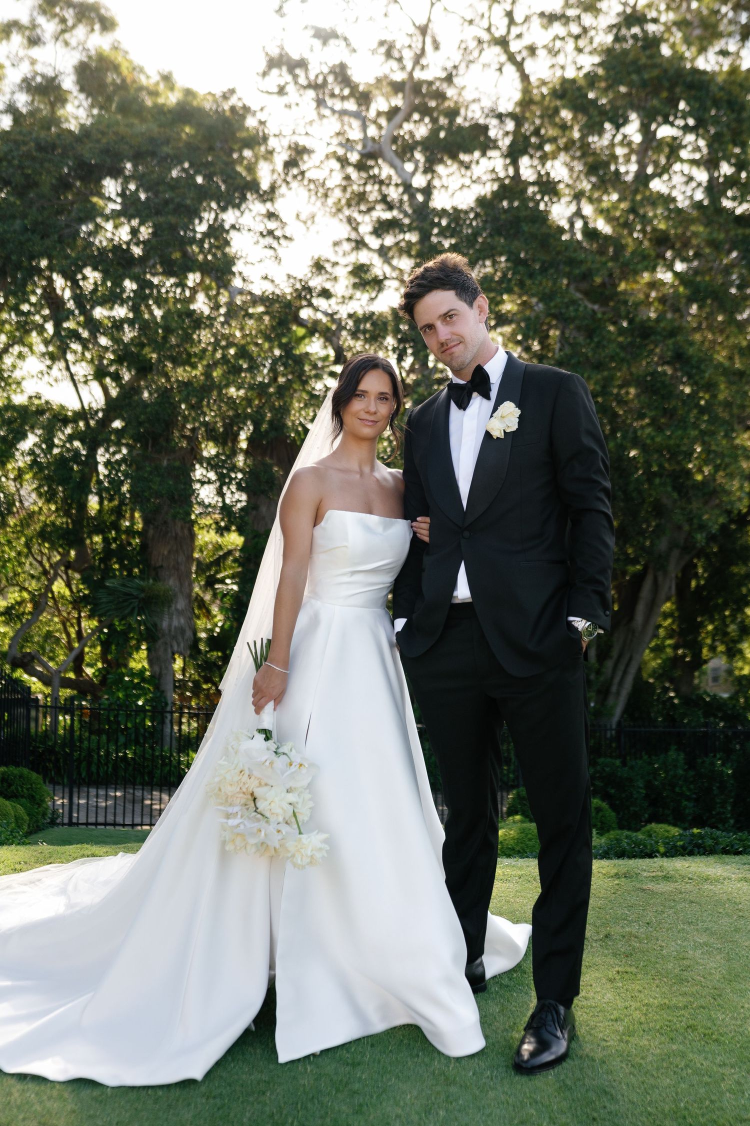 Elegant garden wedding portrait with couple in formal attire against lush greenery.