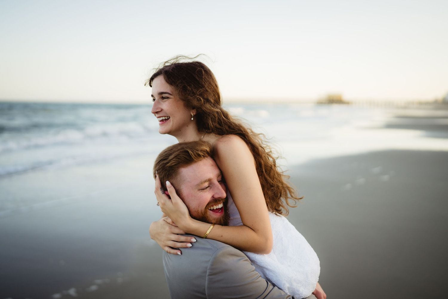 A playful couple embraces on the beach at sunset with natural lighting and laughter.