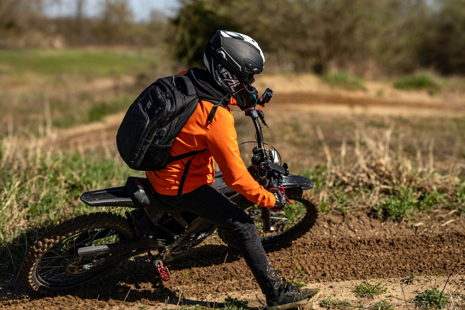 Mountain biker maneuvering through dirt track corner with backpack.