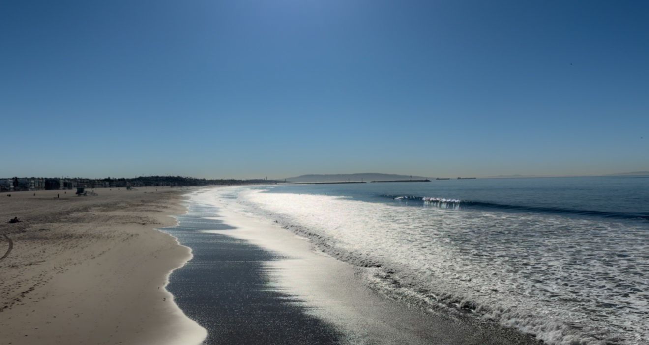 Aerial view of a sandy beach with white waves crashing along the shoreline on a clear blue day.