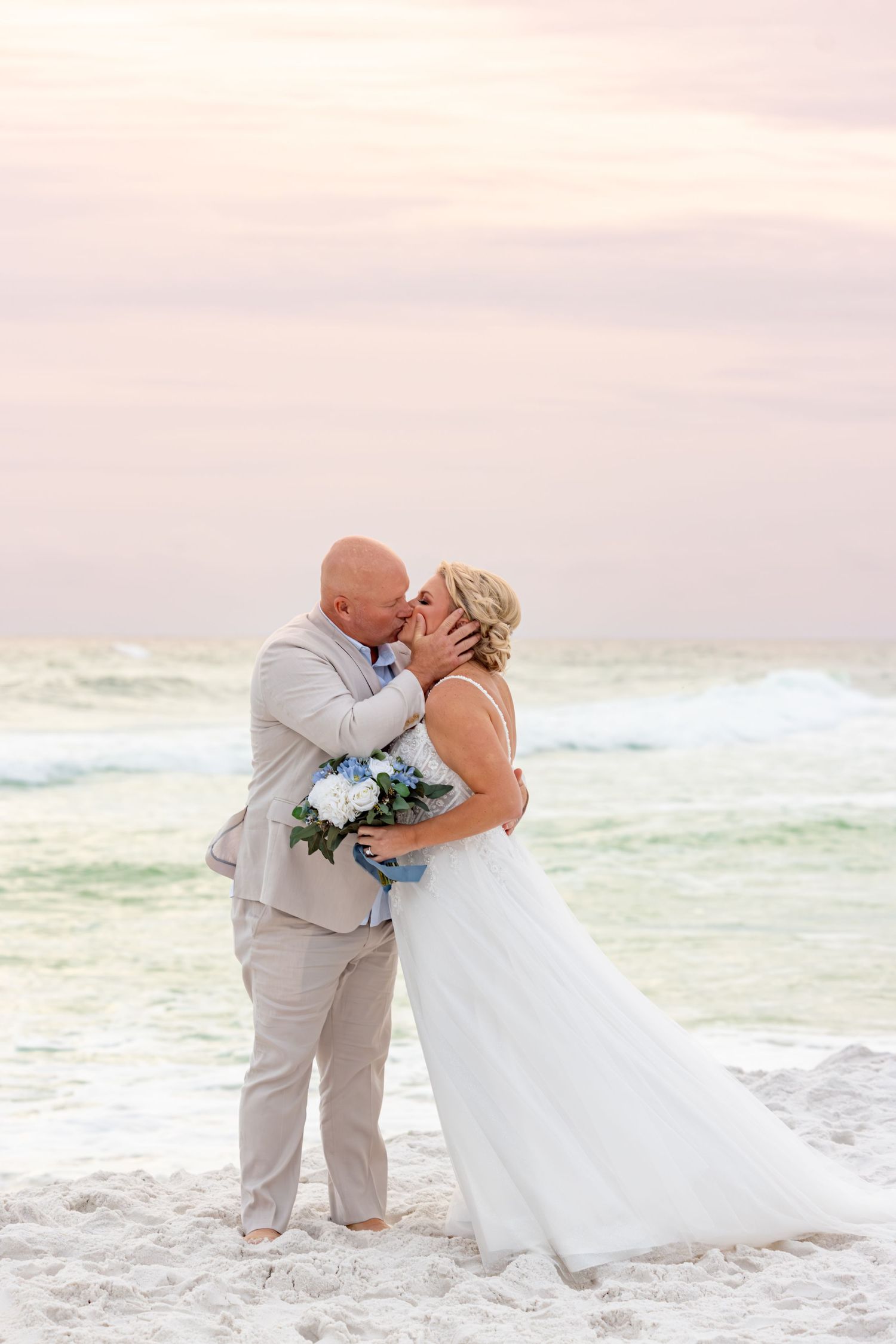 A romantic wedding couple shares intimate moments on a beautiful beach at sunset with crashing waves in the background.