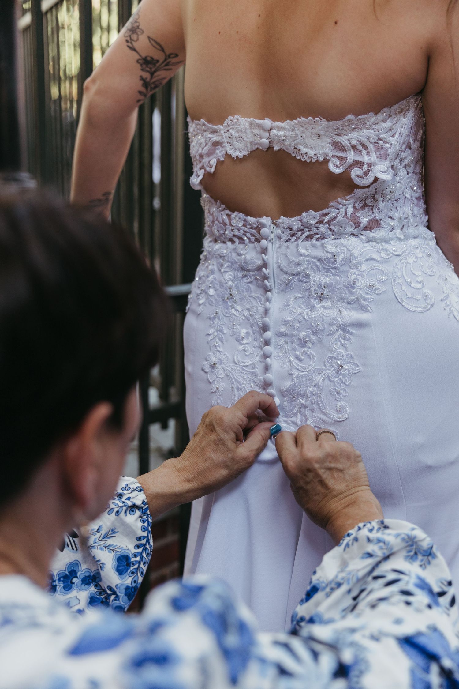 Someone helps adjust the delicate white lace details on the back of a wedding dress during final preparations.