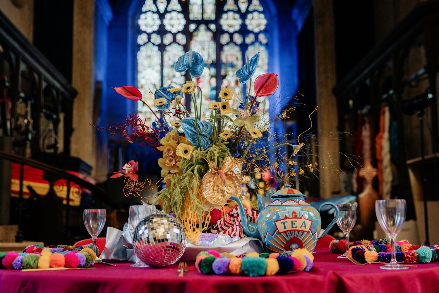 Colorful carnival decorations and festive ornaments adorn a Gothic church interior with stained glass windows.