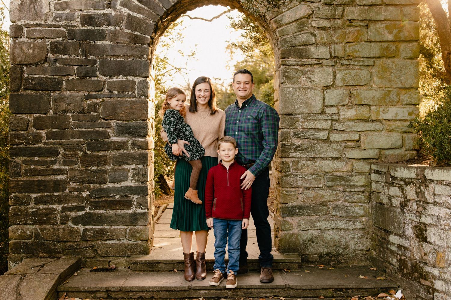 A family poses against a rustic stone wall in an outdoor autumn setting wearing coordinated casual attire in Rockville Maryland