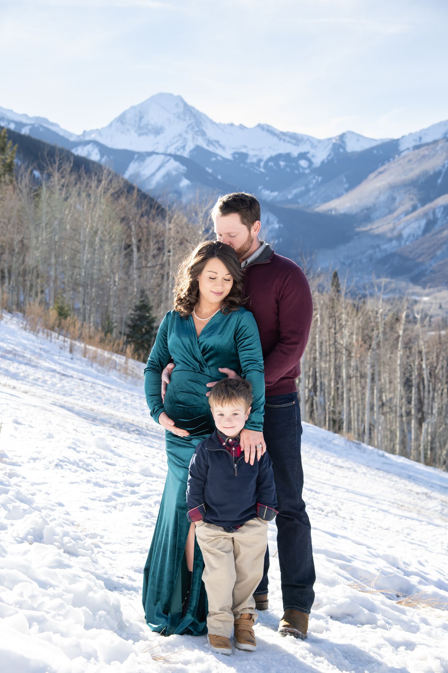 Beautiful winter family photos standing in the snow with mountain peaks and majestic scenery in Aspen Colorado