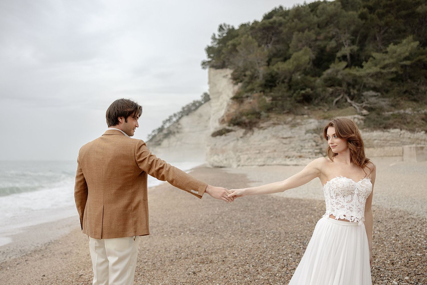 Couple walking along a misty beach shoreline in romantic wedding attire.