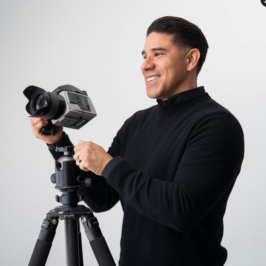 Photographer working with professional camera equipment mounted on a tripod against white background.