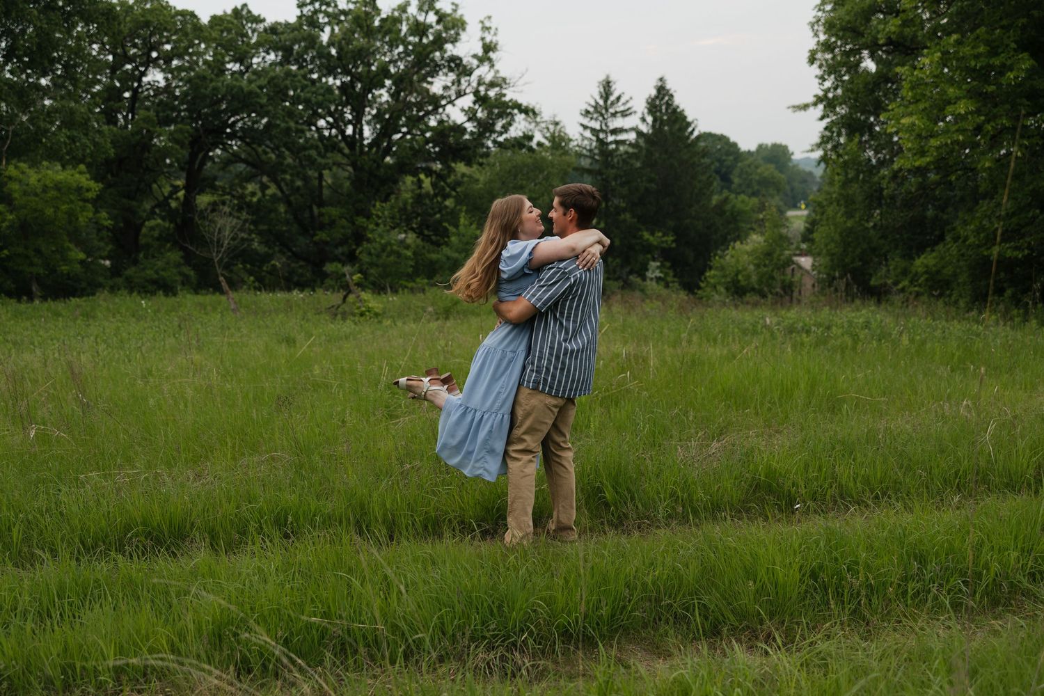 A couple walks hand in hand down a dirt path surrounded by lush summer greenery.