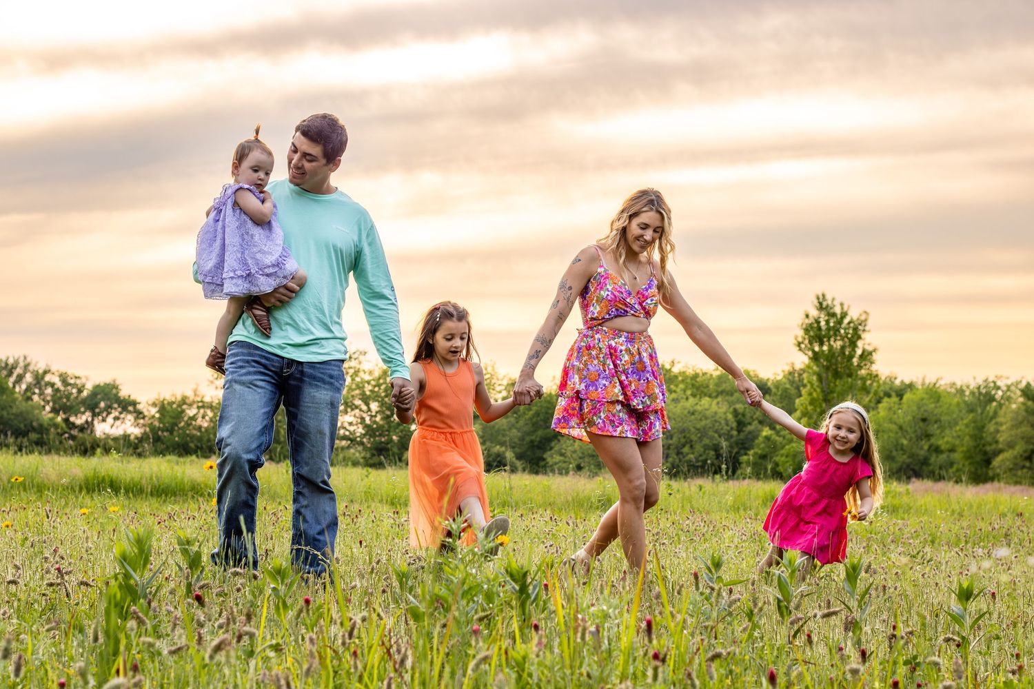 Family enjoying playful moments together in flowering meadow during golden hour.
