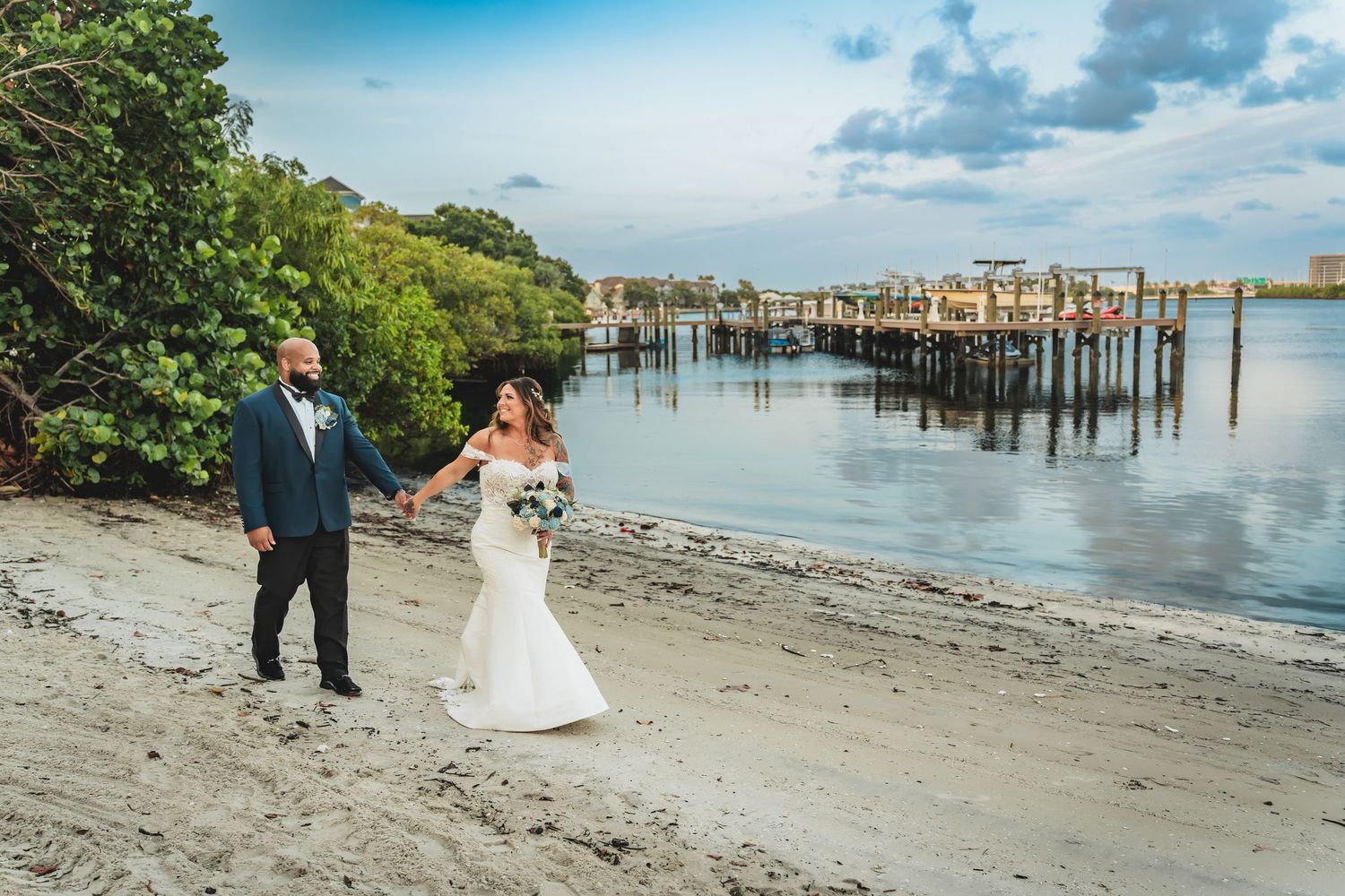 A couple shares romantic moments during their coastal beach wedding photoshoot with wooden docks and water in the background.