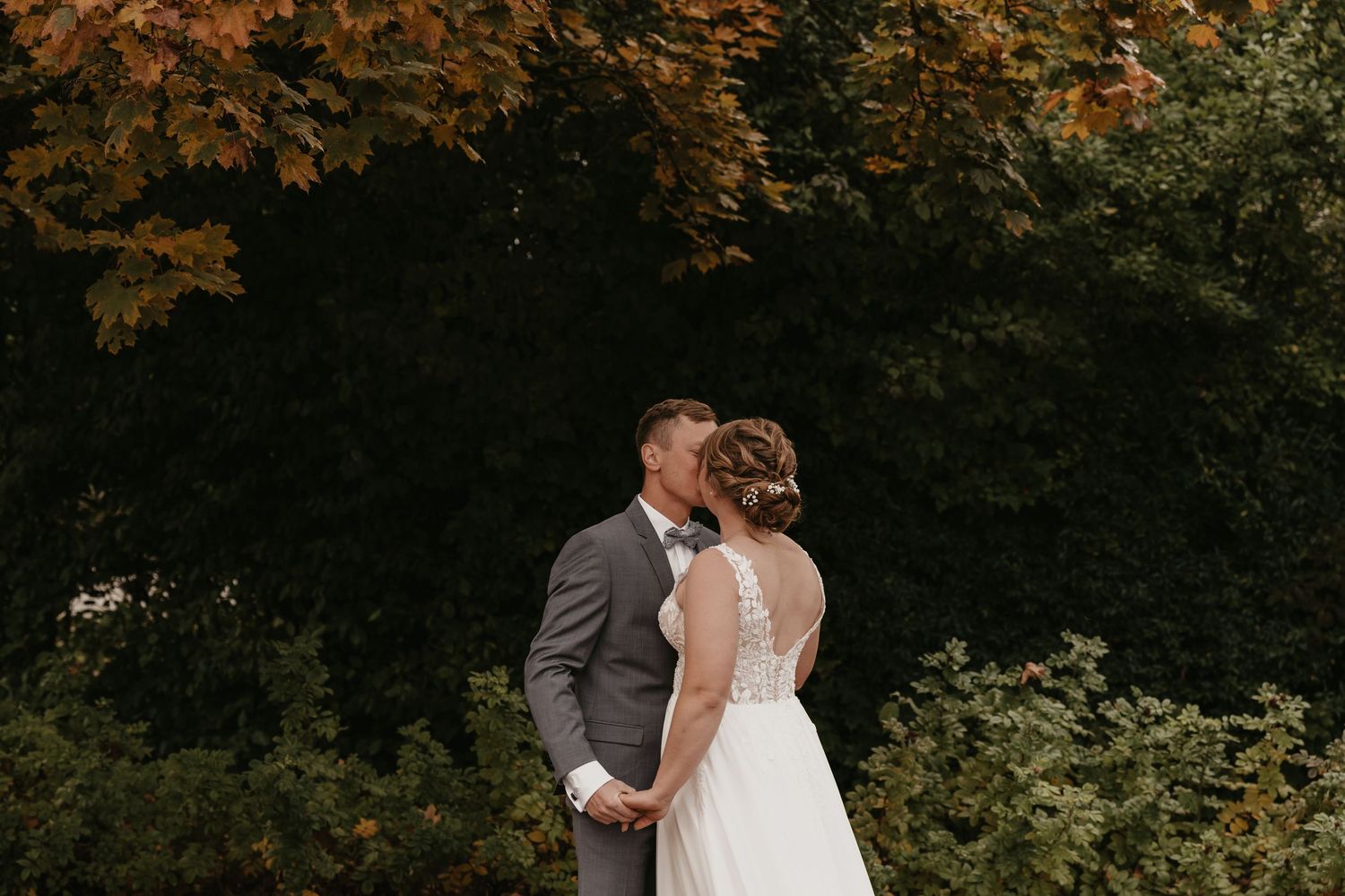 A couple shares romantic moments in a wooded area during their autumn wedding photoshoot.