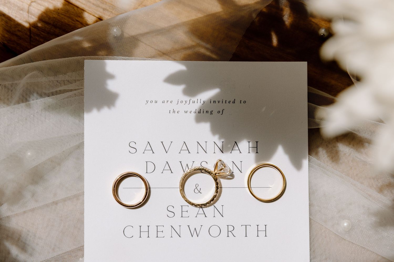 Golden wedding rings casting delicate shadows on a textured white surface with decorative elements nearby.
