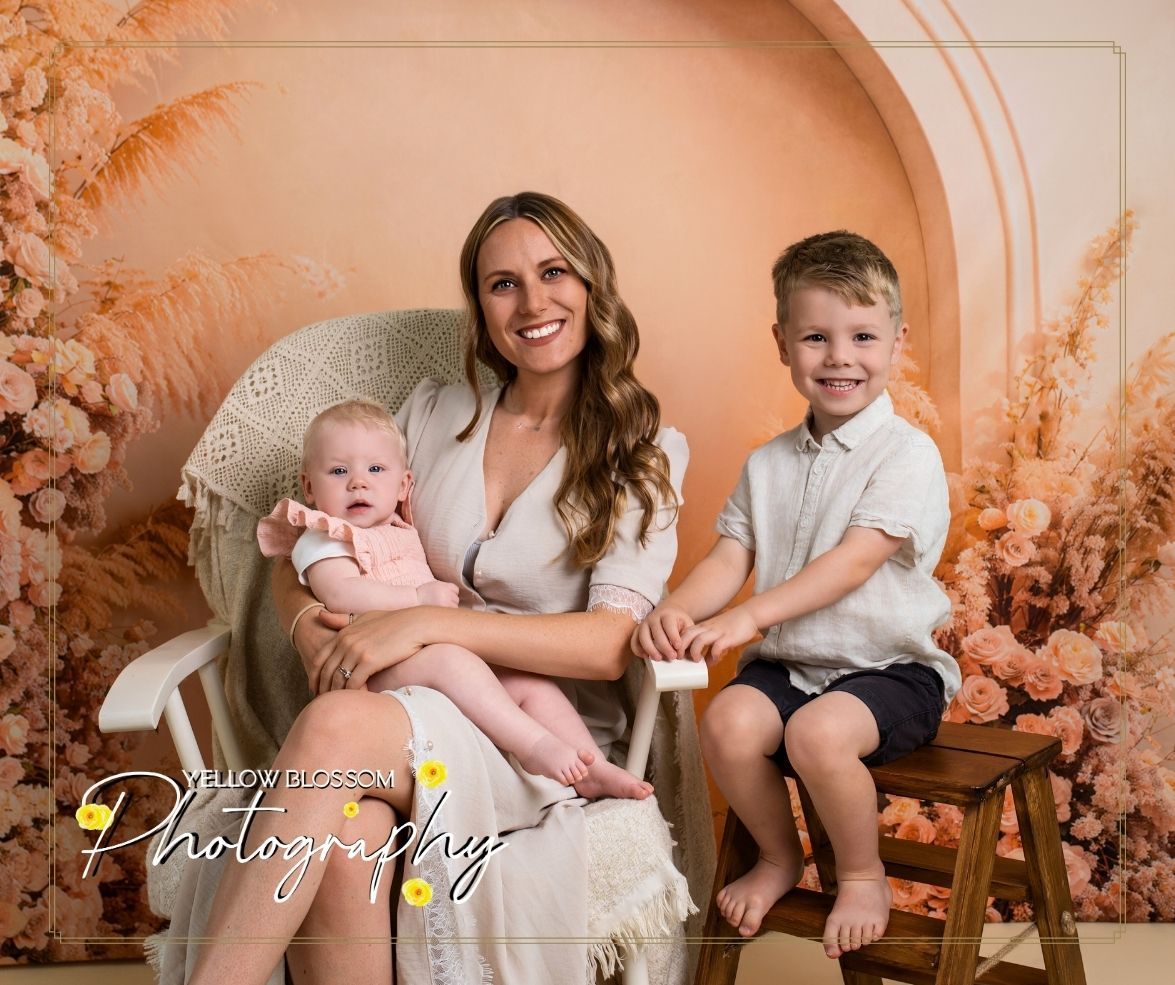 Family sitting together in a peach-colored studio with floral decorations and soft lighting during a photo session.