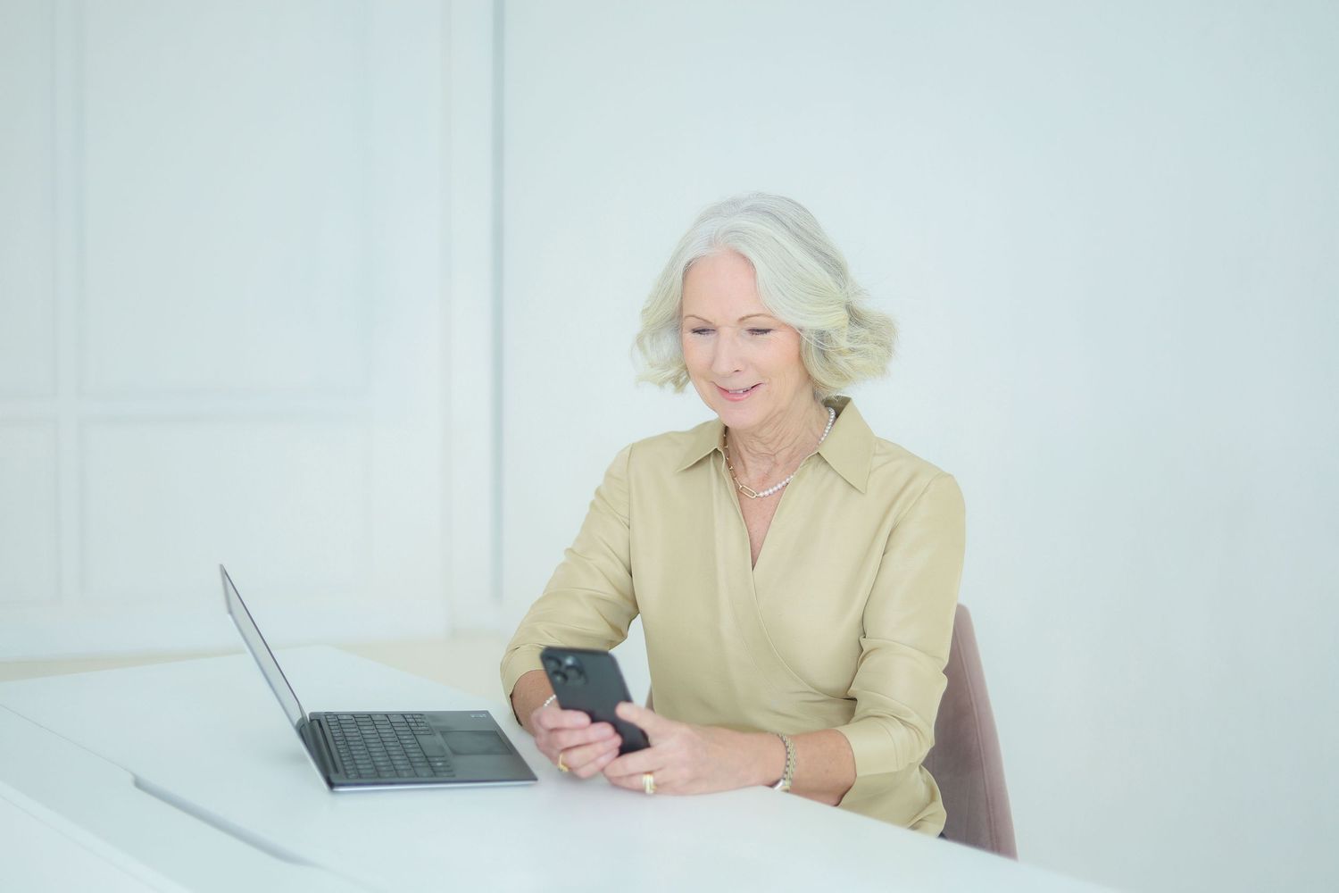 Woman working on laptop and mobile phone in bright minimalist office space.
