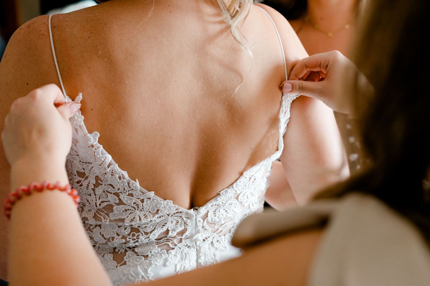 A bridesmaid carefully fastens the delicate lace straps of a bride's wedding dress.