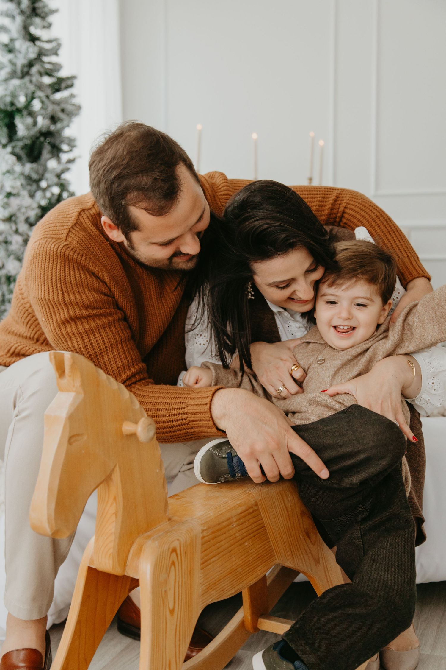 A family shares tender moments of affection and laughter while sitting together on a wooden chair during a holiday photoshoot.