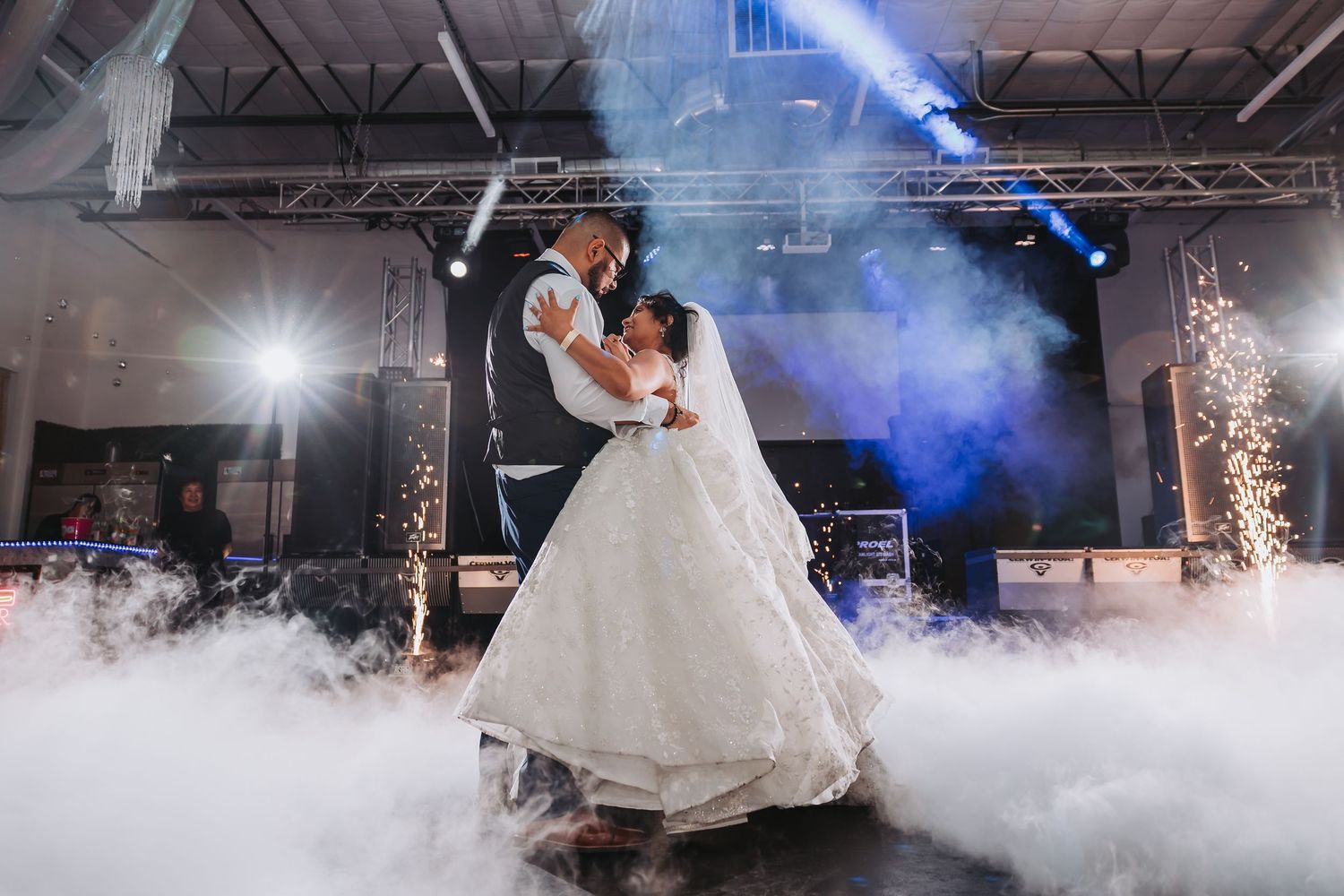 Newlyweds dance on a misty dance floor with dramatic blue lighting and sparklers creating a magical atmosphere.