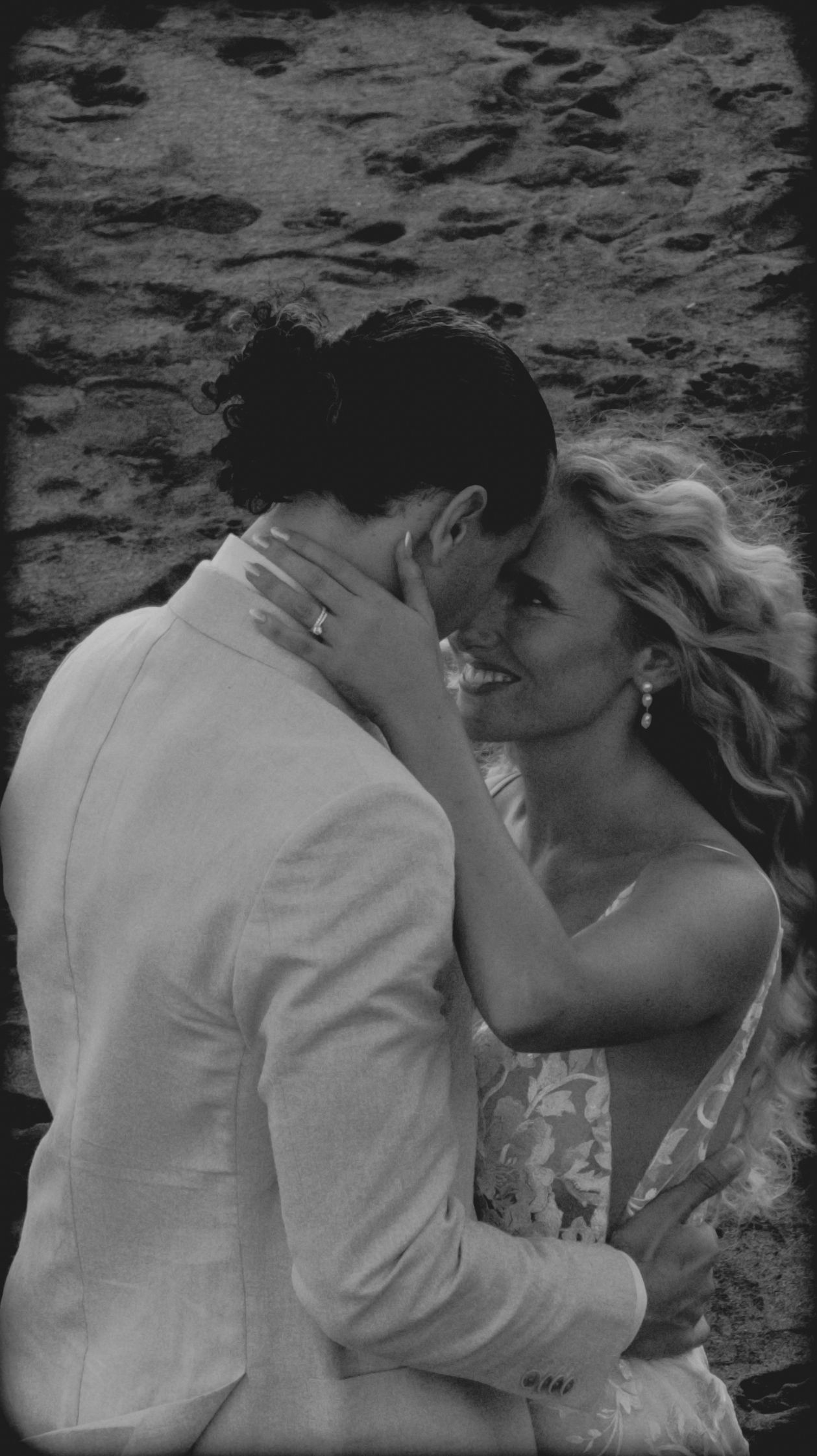 Silhouetted couple sharing a romantic kiss under flowing wedding veil at sunset with dramatic sky in background.