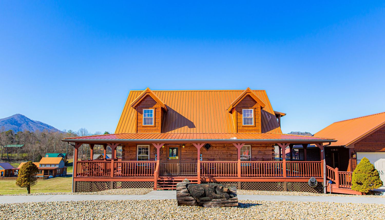 Modern rustic log cabin resort buildings with orange roofs set against bright blue sky in mountain landscape.