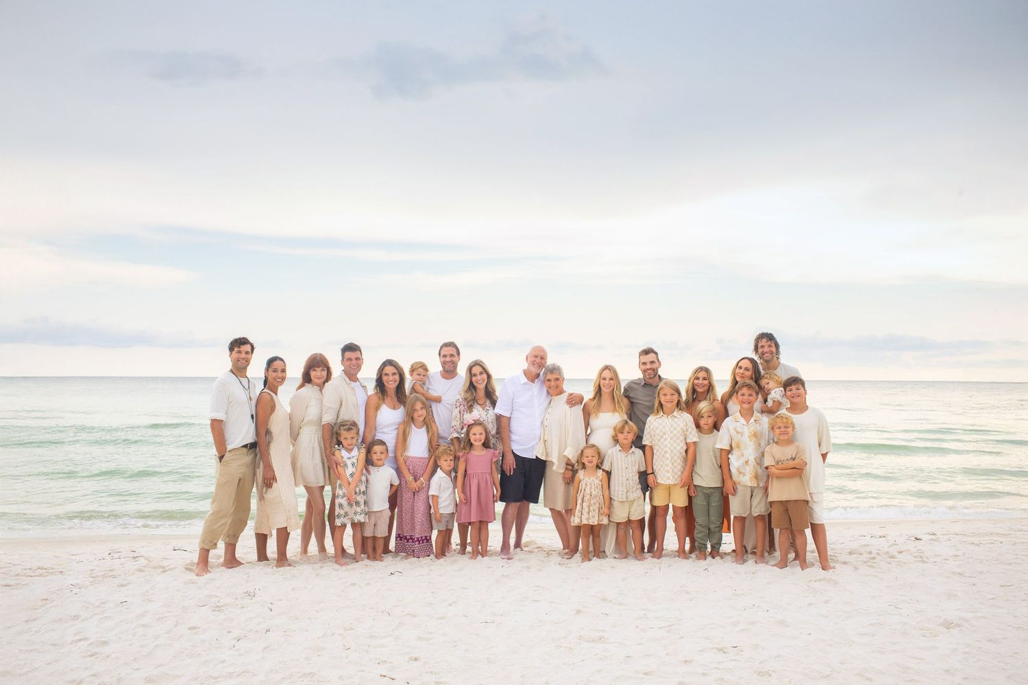 A family wearing white outfits shares a playful moment together on a sandy beach.