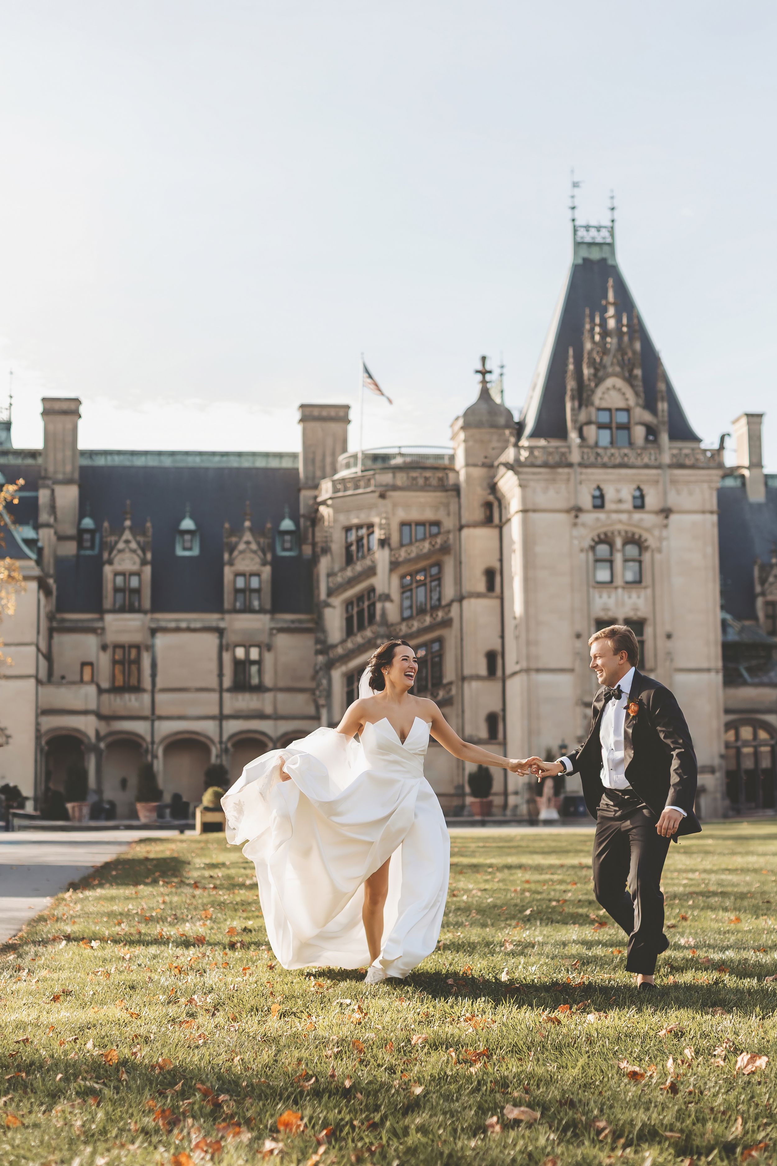 A couple runs playfully on the lawn in front of the majestic Biltmore Estate in Asheville, North Carolina.