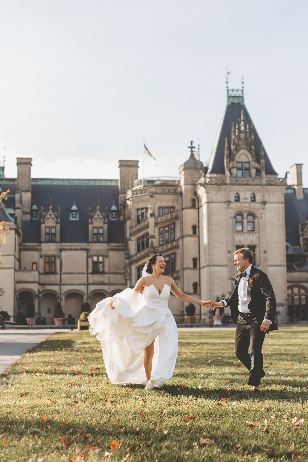A couple runs playfully on the lawn in front of the majestic Biltmore Estate in Asheville, North Carolina.