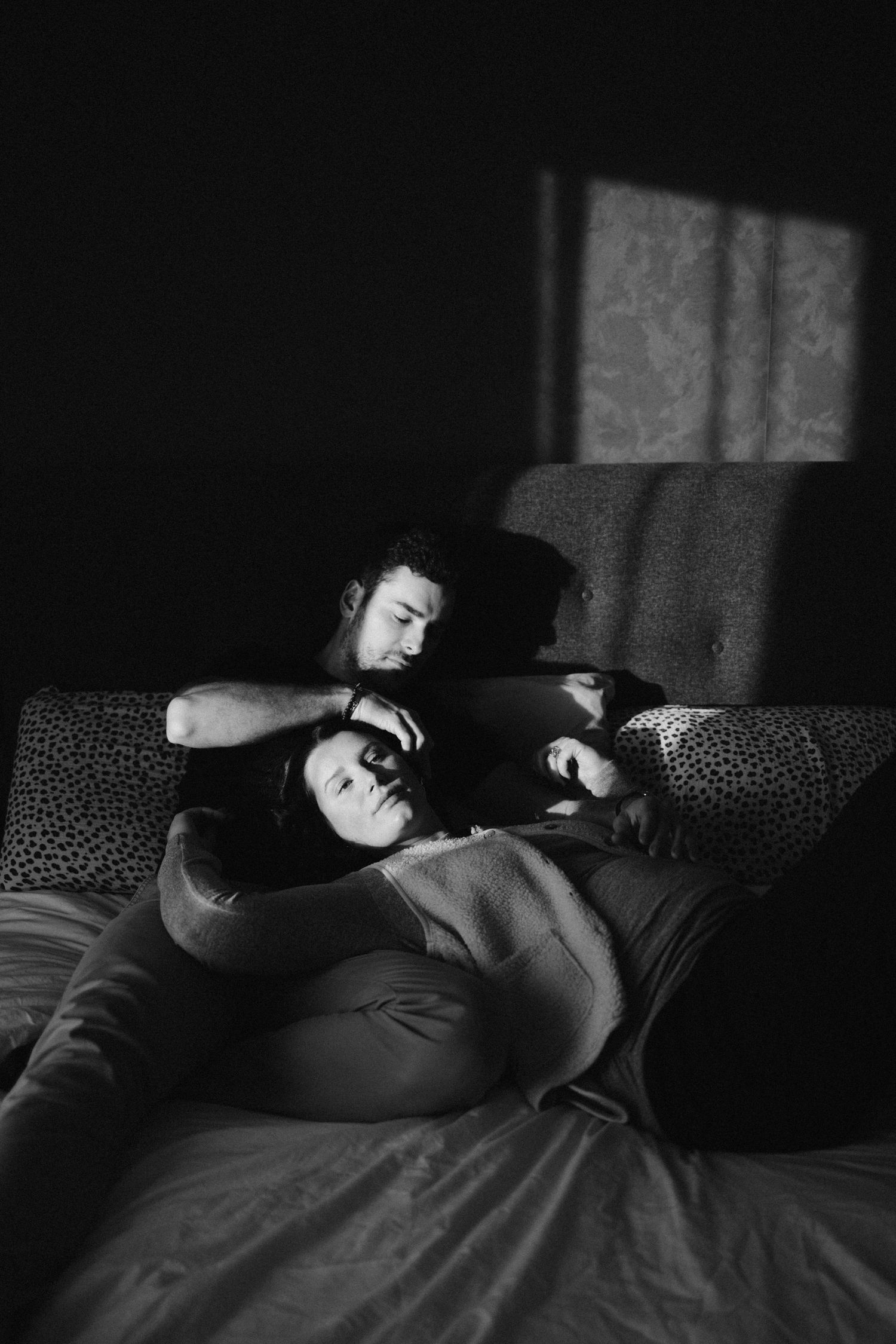 A couple shares an intimate moment while relaxing together on a grey couch in a dimly lit room.