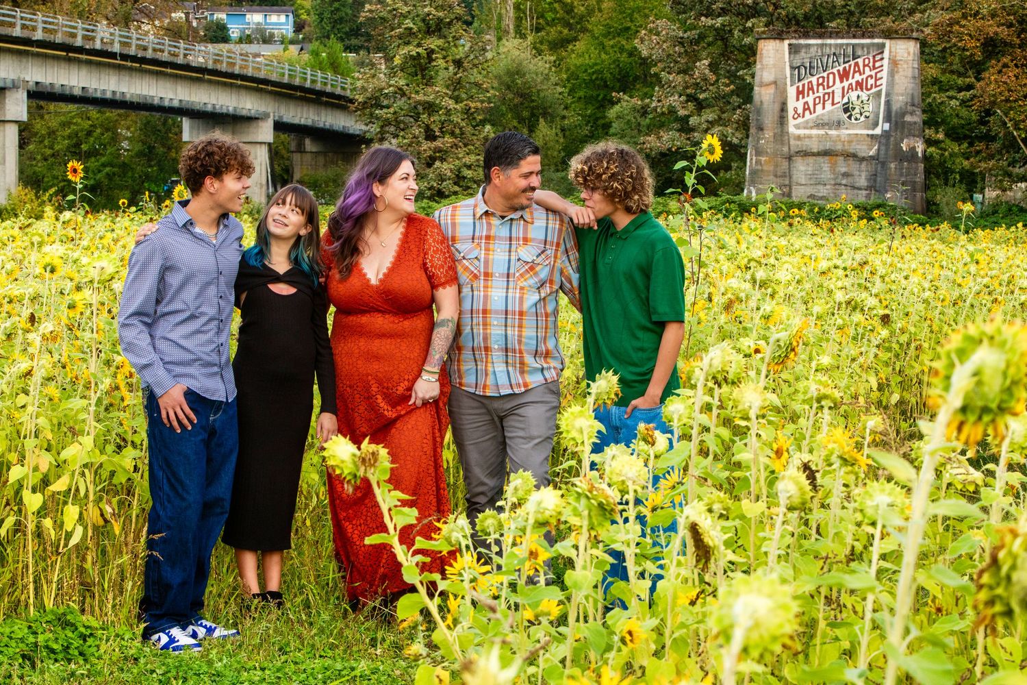 Family holding hands in a sunflower field with green hills, children between parents in a joyful outdoor portrait.
