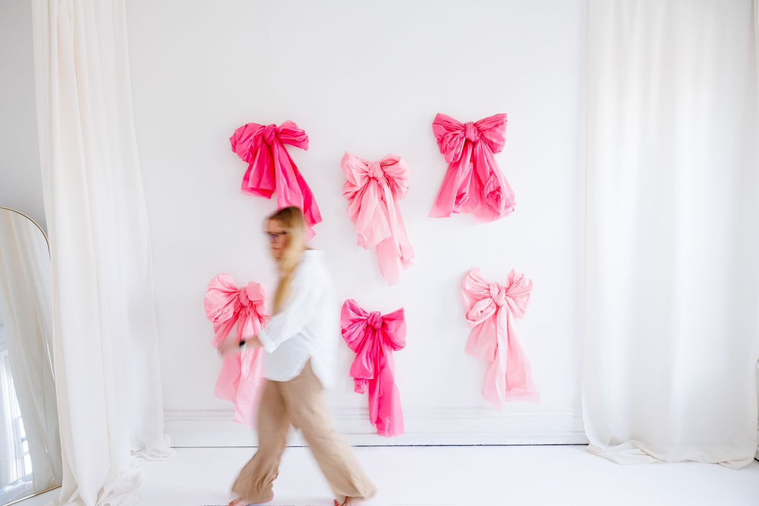 Pink bows and ribbons decorate a white wall while a person in white clothing stands to the side.