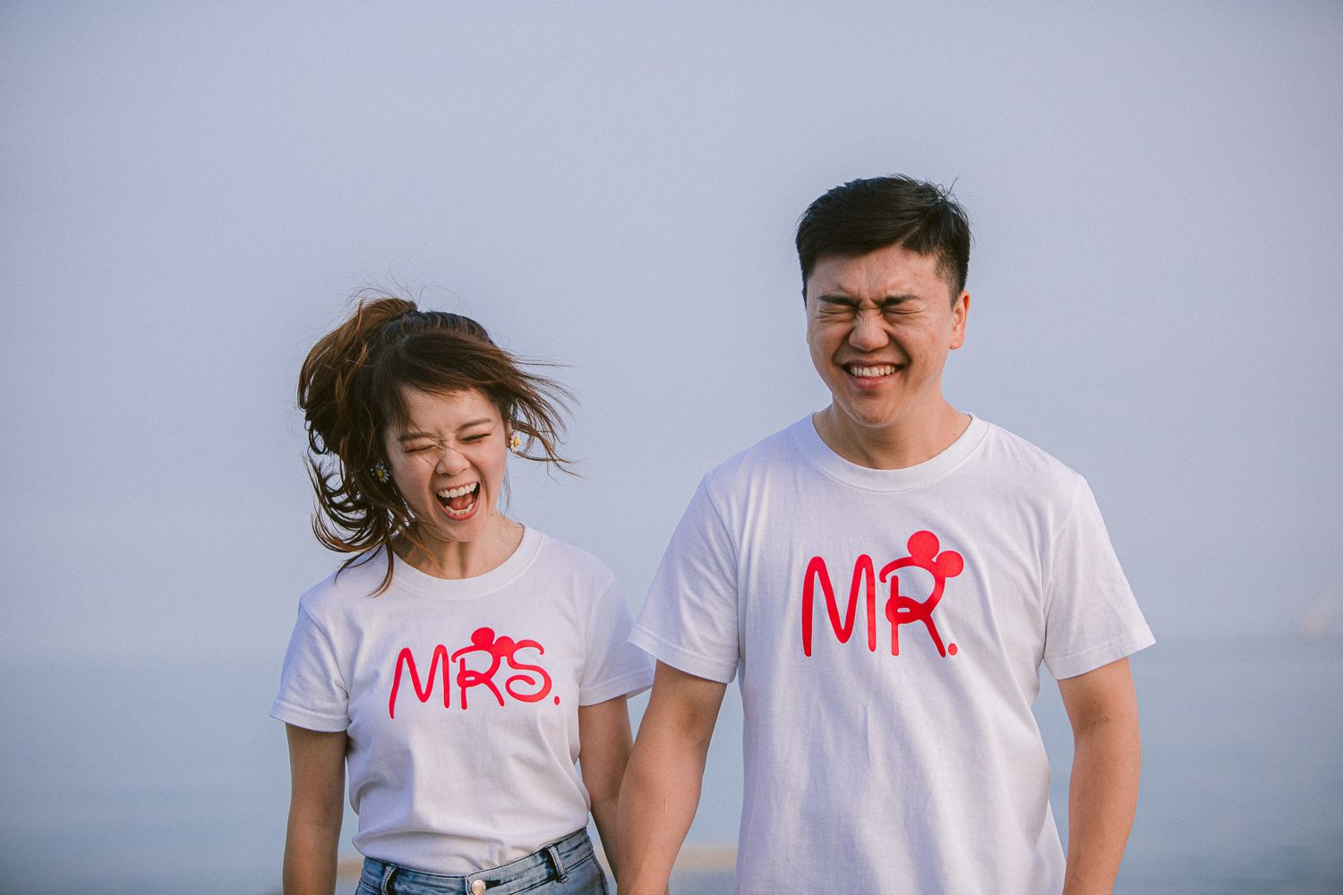 A couple in matching white t-shirts with Mr and Mrs text embrace and laugh together outdoors.