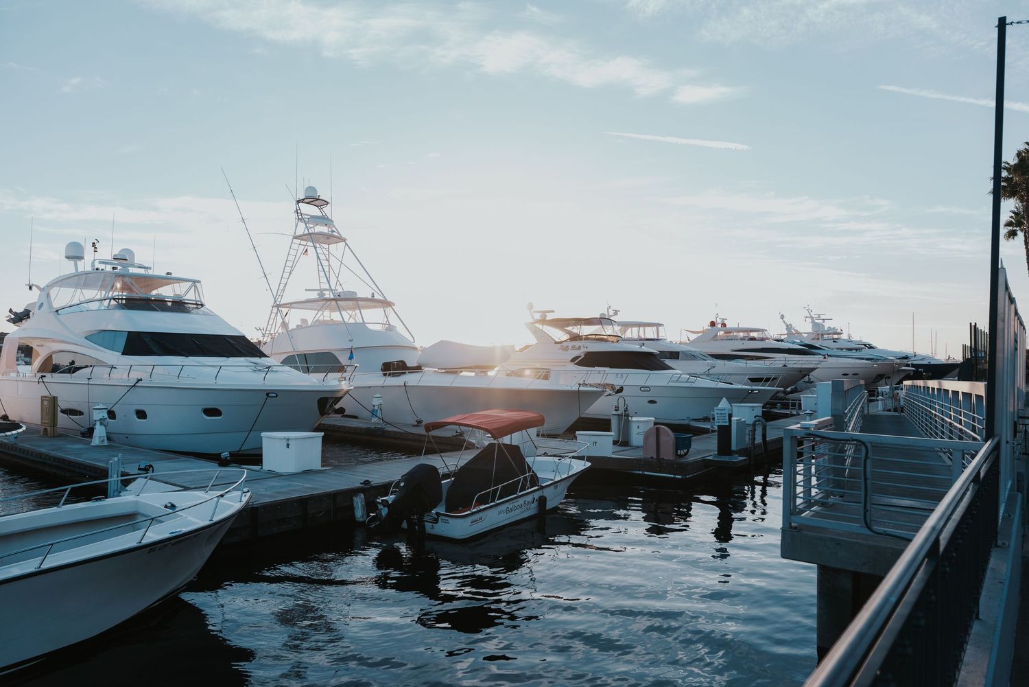 Luxury yachts and fishing boats docked at a marina during sunset with reflections on calm water.