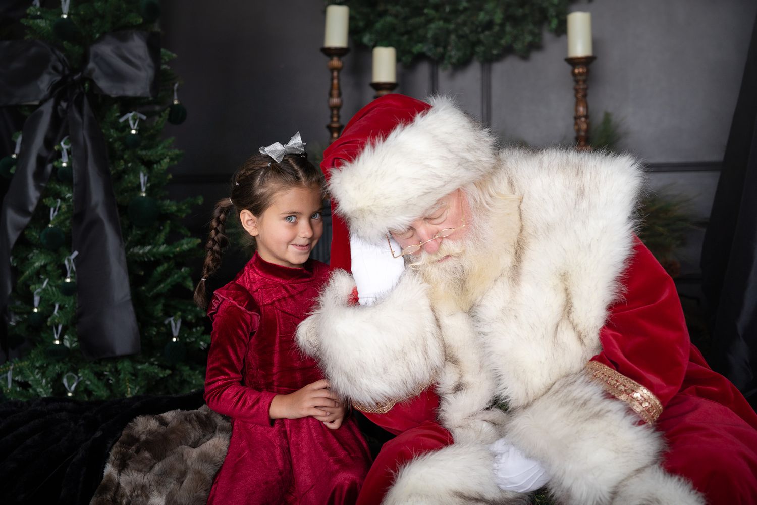 Several kids meet with Santa Claus near a decorated Christmas tree at what appears to be a holiday photo session.