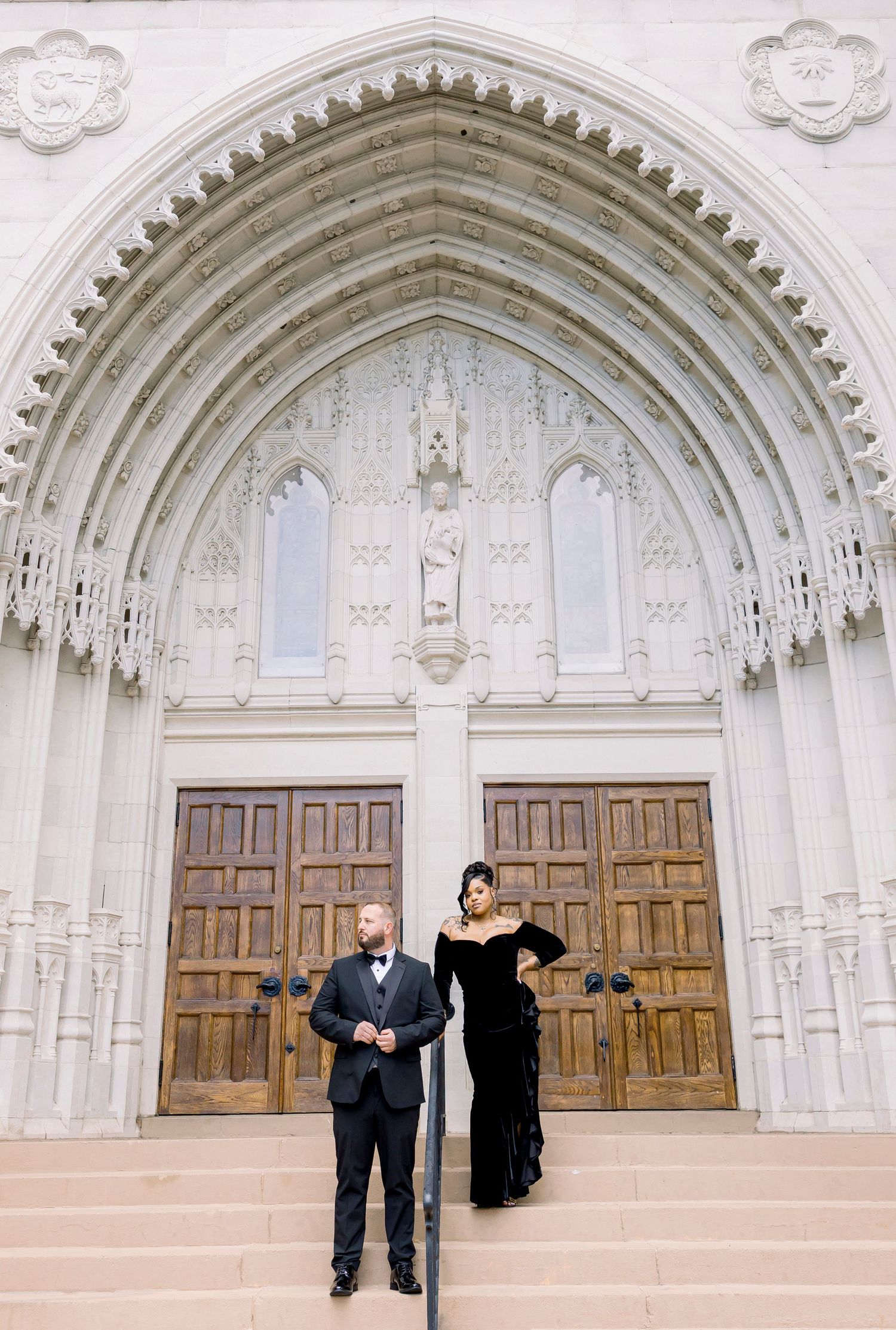 Two people pose for a series of fun photos against the backdrop of an ornate white gothic church entrance archway.
