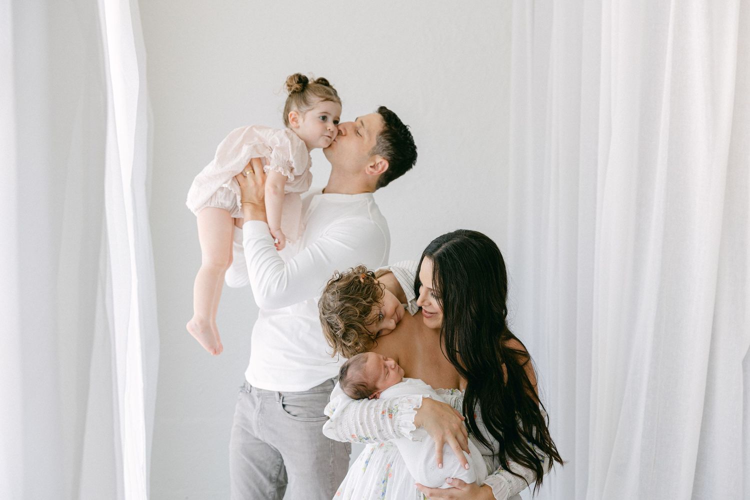 A family in white outfits shares joyful moments together against a bright white backdrop. Hartford Newborn Photography Studio.