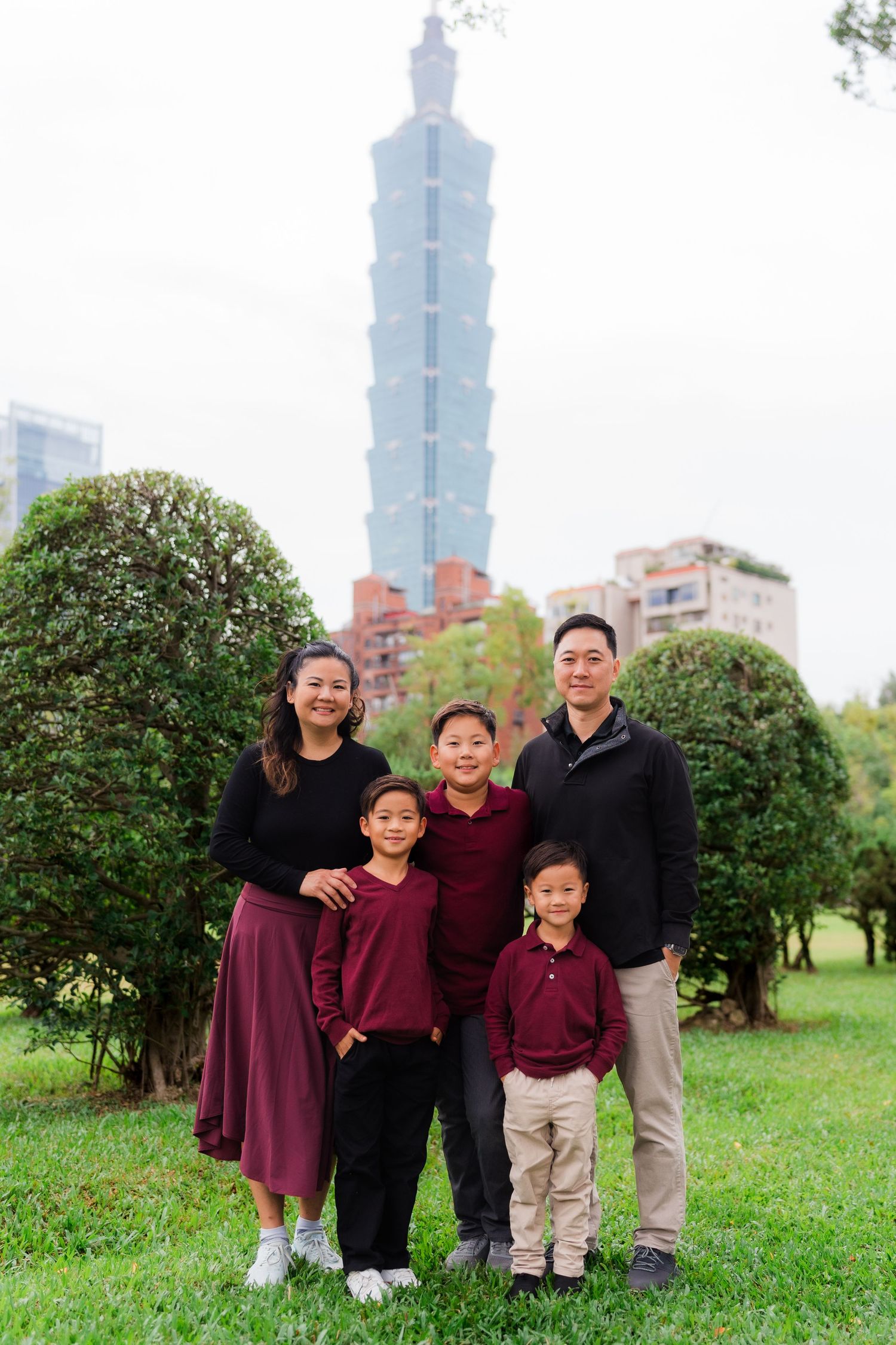 A family poses together on a grassy hill with the Taipei 101 skyscraper visible in the background.