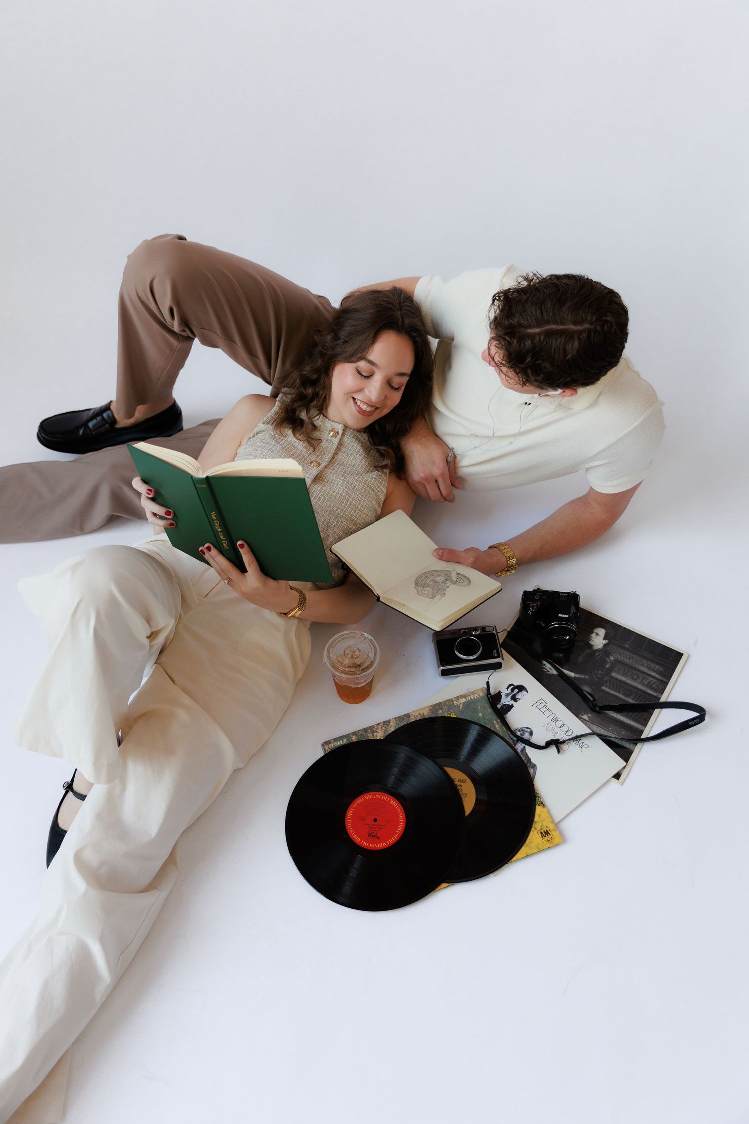Person in white outfit lying on floor listening to vinyl records on turntable in minimalist setting.