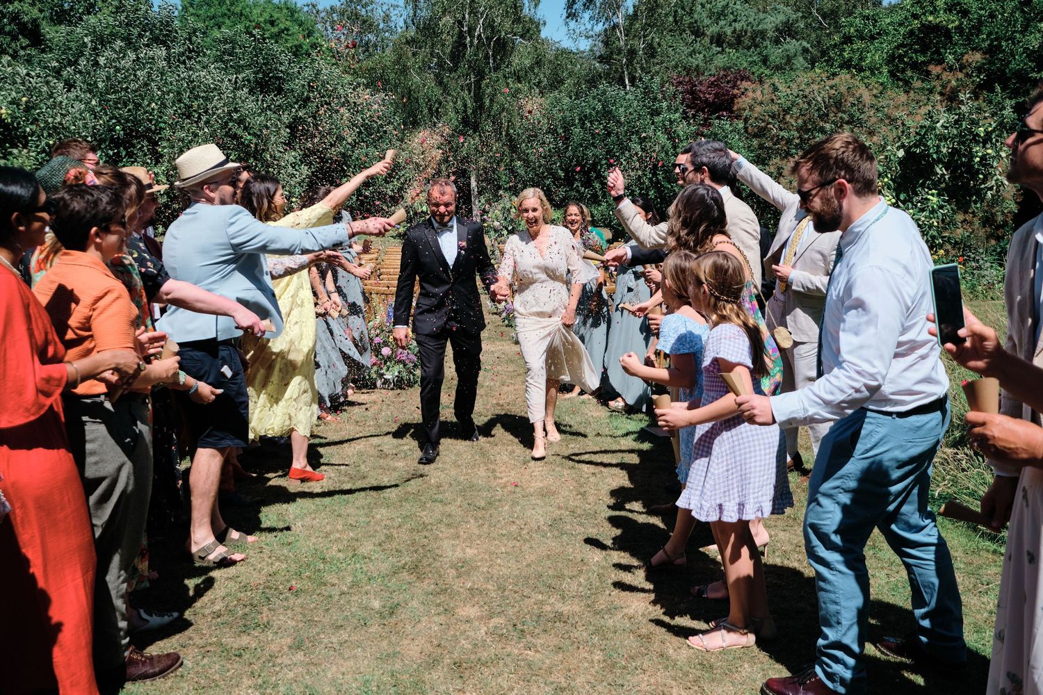 A line of people stand outside in a grassy area performing group activities at a wedding.