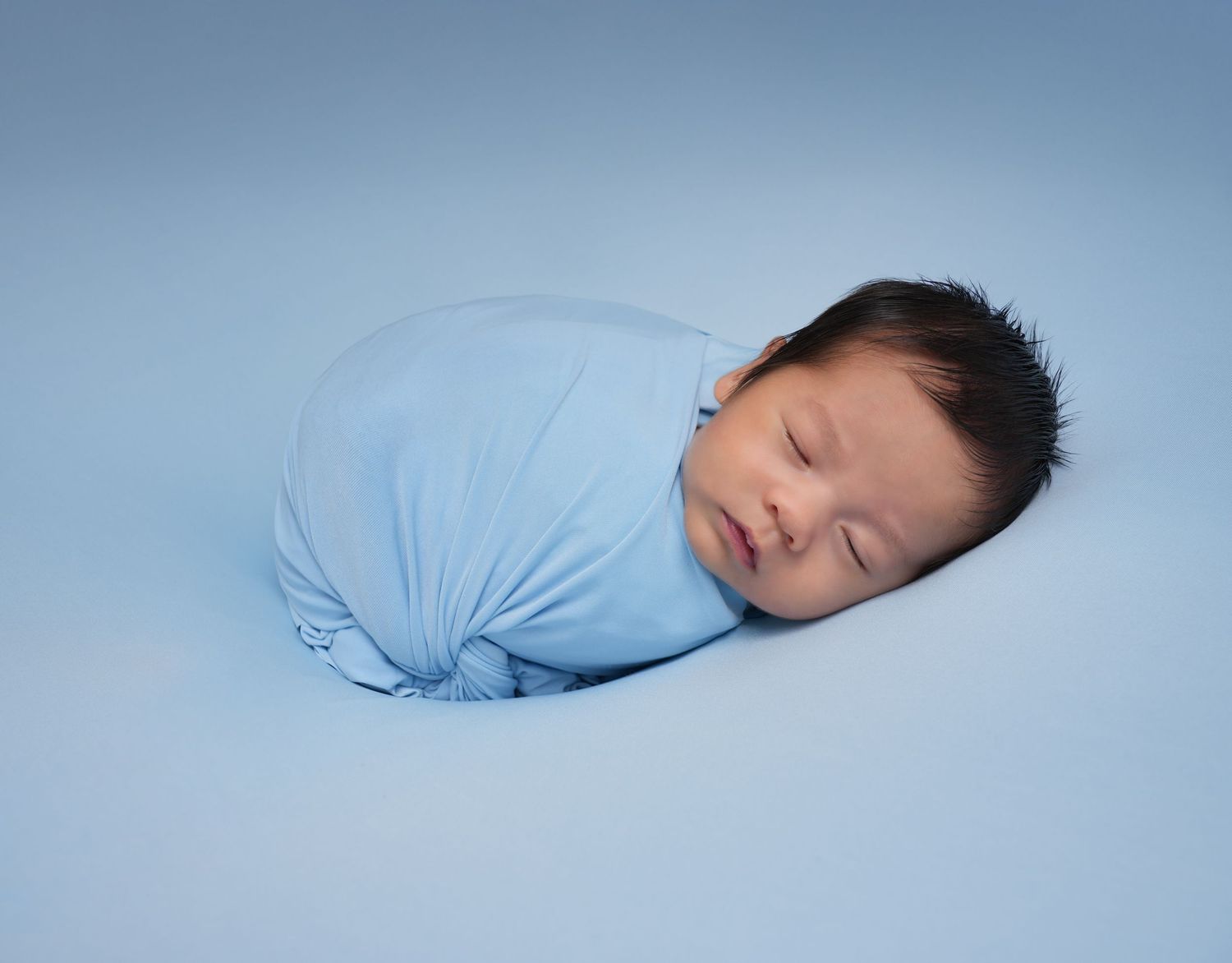 A collage of baby photography showing a sleeping infant in various poses against soft blue backgrounds and wraps.