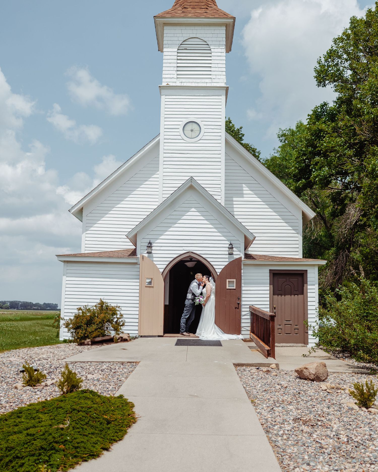 A series of white country church exteriors with brown accents and walkways surrounded by rock landscaping.