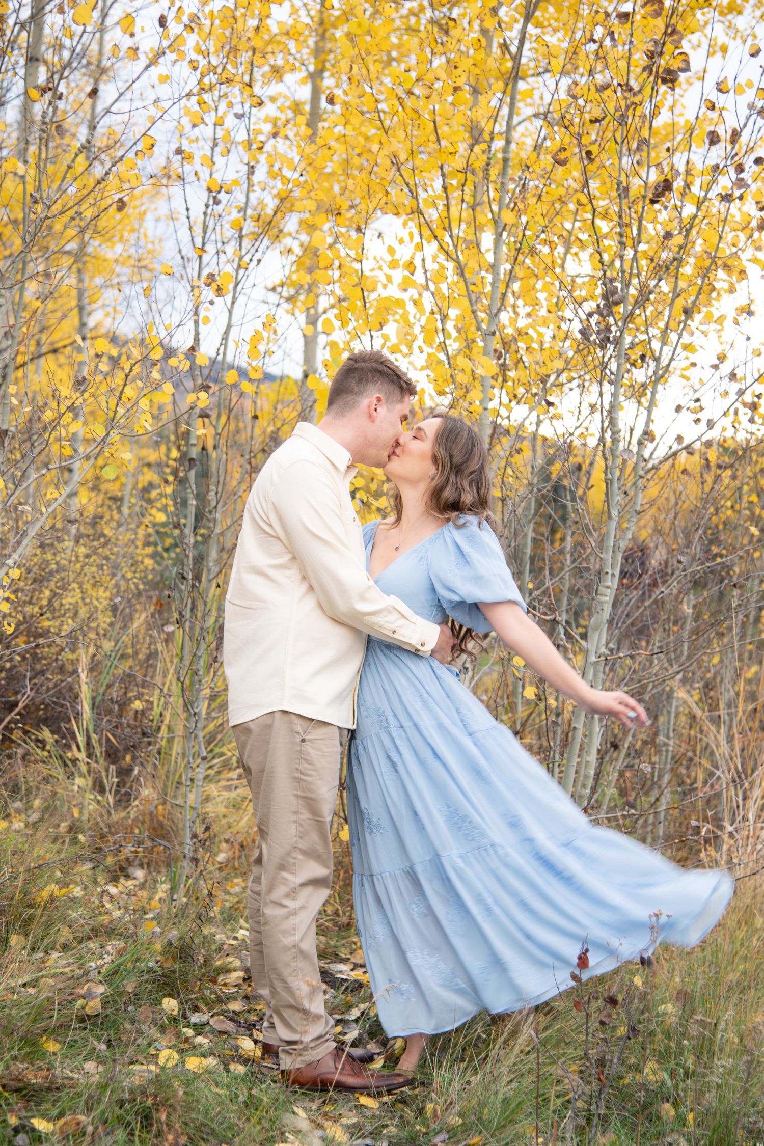 A couple in autumn attire dances romantically among golden aspen trees during a fall photoshoot.