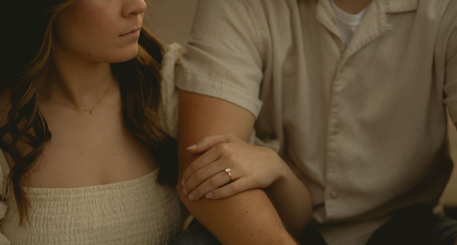 Close-up of couple with woman wearing diamond engagement ring on her hand resting on mans arm.