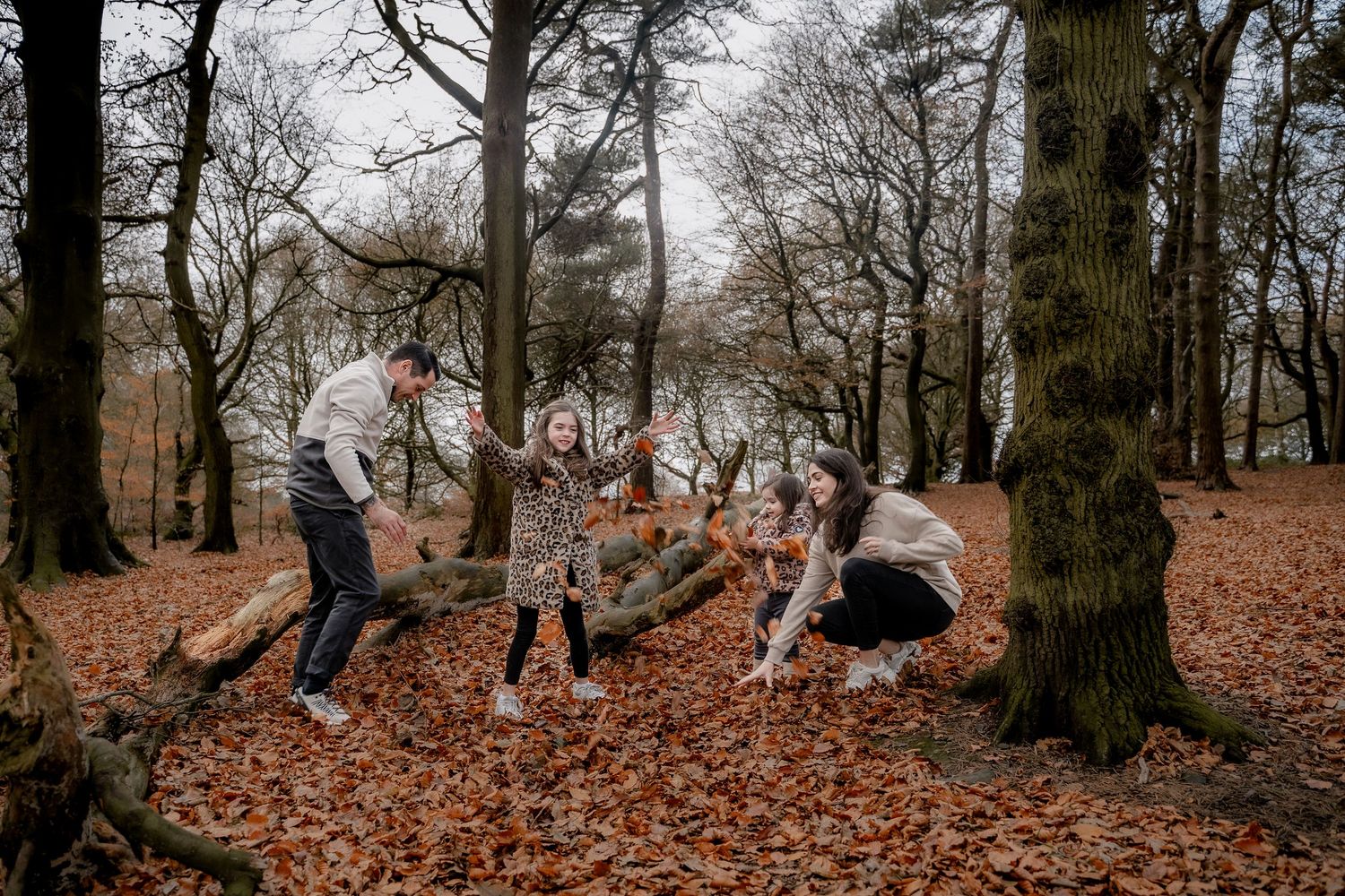 Parents and children laughing together under golden autumn trees during lifestyle photoshoot.