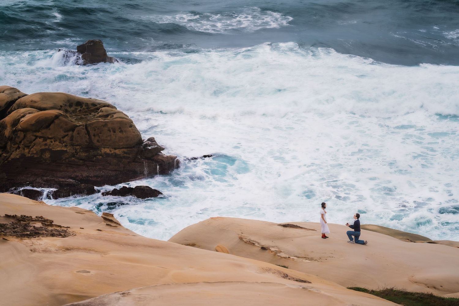 Aerial view of a rugged coastline with crashing waves against rocky cliffs and sandy beaches in dramatic lighting.