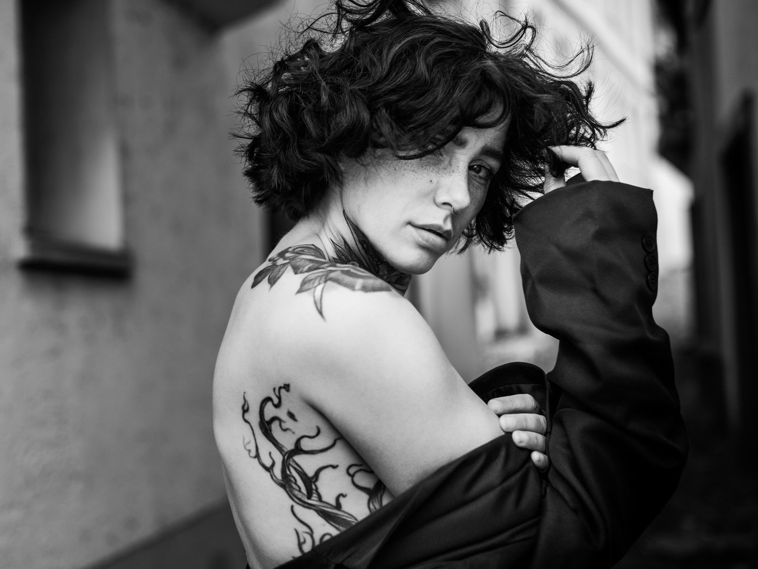 Black and white portrait of woman with curly hair and back tattoo.