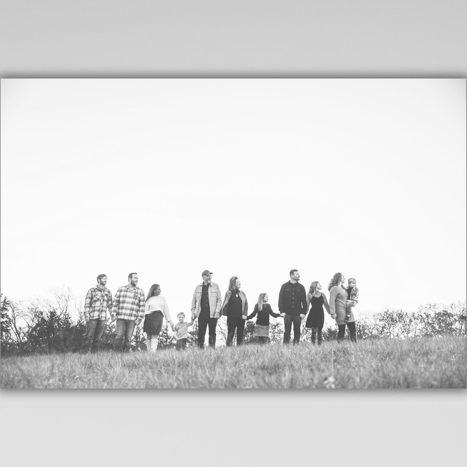 A black and white panoramic photograph shows a group of people standing in a field against a light sky.